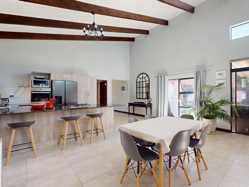 Spacious open-plan living and kitchen area featuring high vaulted ceilings with exposed timber beams, granite countertops, and direct access to the outdoor patio.