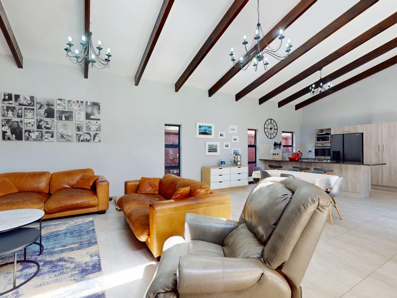 Spacious open-plan living and kitchen area featuring high vaulted ceilings with exposed timber beams, modern cabinetry, and tiled flooring throughout.