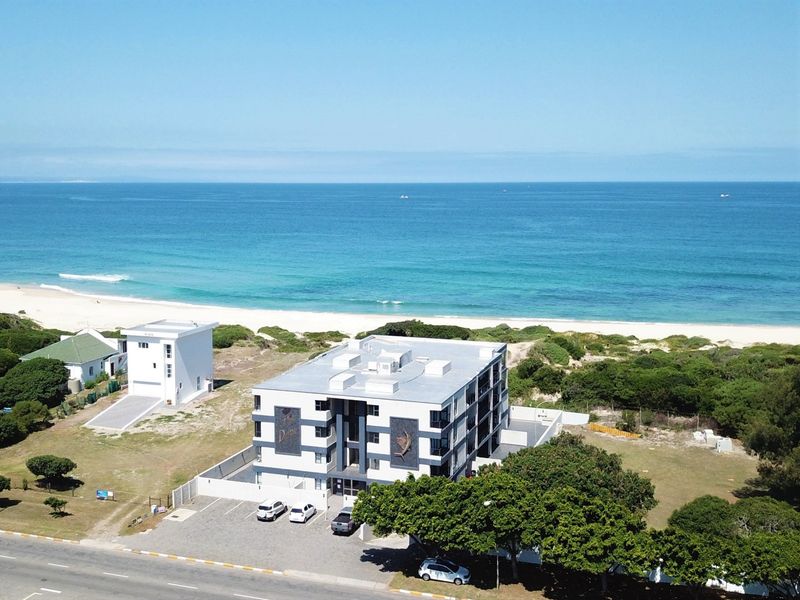 Aerial view of a modern apartment complex situated directly adjacent to the coastline and beach.