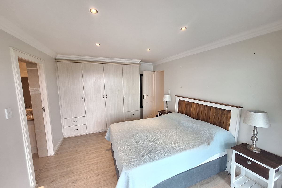 A well-maintained bedroom featuring light-toned laminate flooring, built-in cupboards, and recessed ceiling downlights, with an adjoining bathroom entrance.
