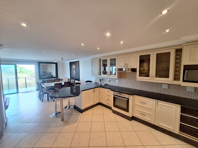 Spacious open-plan kitchen and dining area featuring classic cabinetry, granite countertops, integrated appliances, and direct access to a balcony with scenic views.