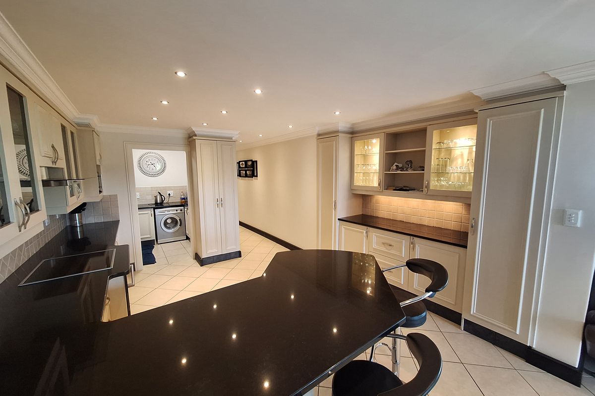 Modern kitchen featuring high-quality cabinetry, granite countertops, integrated breakfast bar, and recessed lighting, with an adjacent laundry area visible.