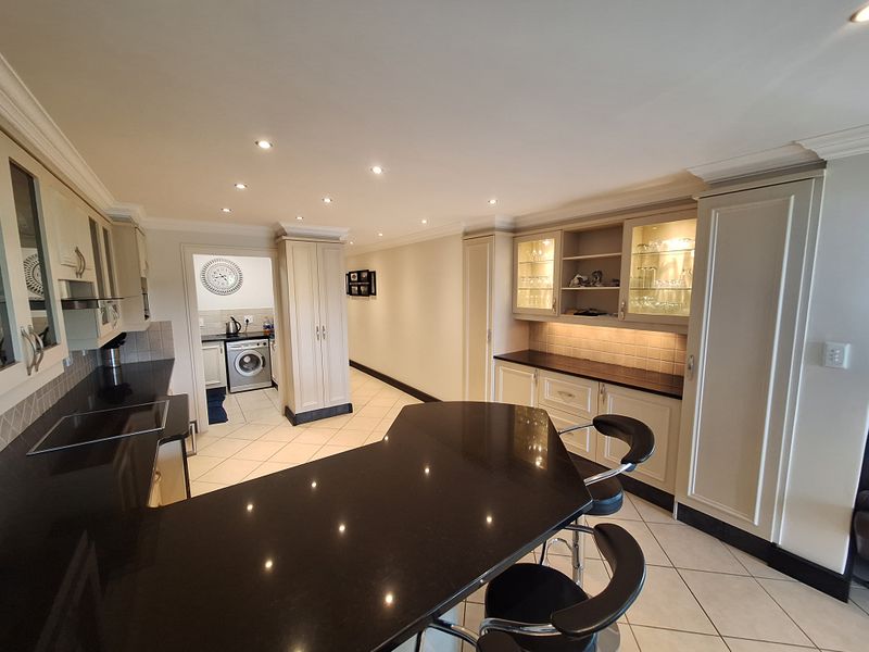 Modern kitchen featuring high-quality cabinetry, granite countertops, integrated breakfast bar, and recessed lighting, with an adjacent laundry area visible.
