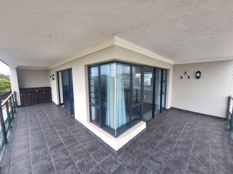 Spacious covered balcony featuring dark tiled flooring, built-in cabinetry, and large glass sliding doors with a corner window design.