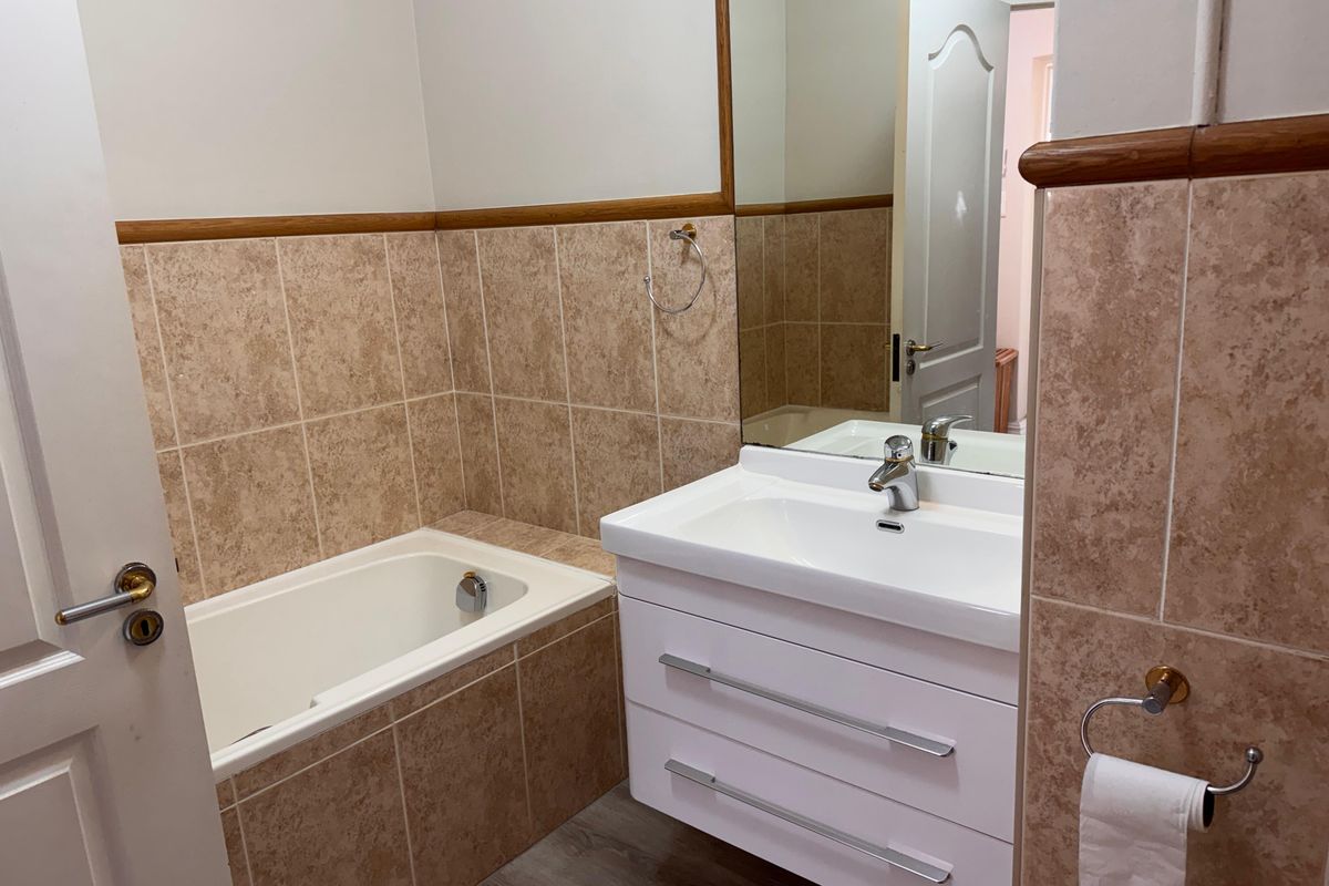 A clean, functional bathroom featuring a built-in bathtub, modern white vanity cabinet, and neutral ceramic wall tiling.