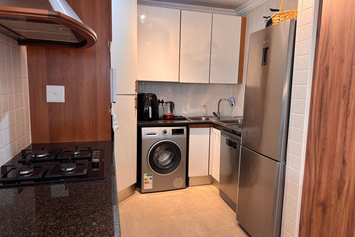 Compact kitchen featuring granite countertops, white cabinetry, tiled backsplash, gas hob with extractor, and integrated appliances including a dishwasher and washing machine.