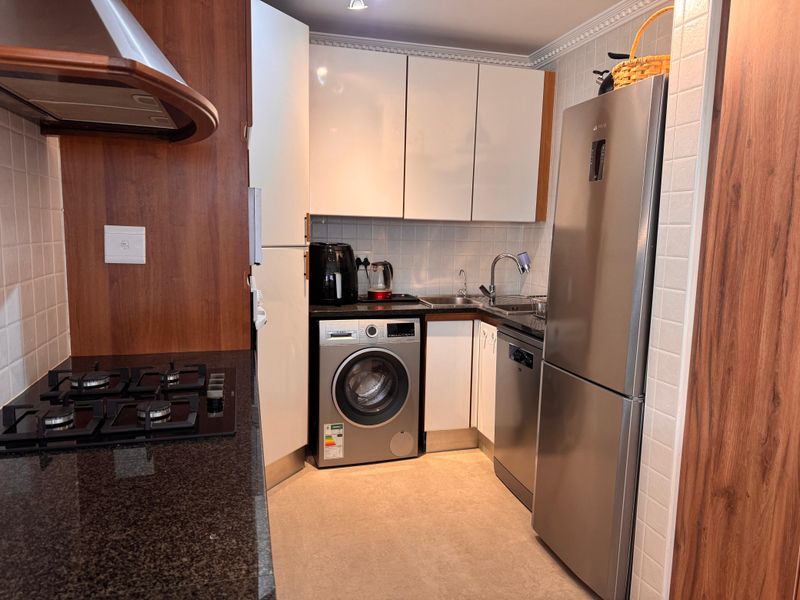 Compact kitchen featuring granite countertops, white cabinetry, tiled backsplash, gas hob with extractor, and integrated appliances including a dishwasher and washing machine.