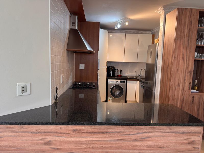 A compact, modern kitchen featuring granite countertops, a gas hob with extractor fan, built-in cabinetry, and an integrated washing machine.