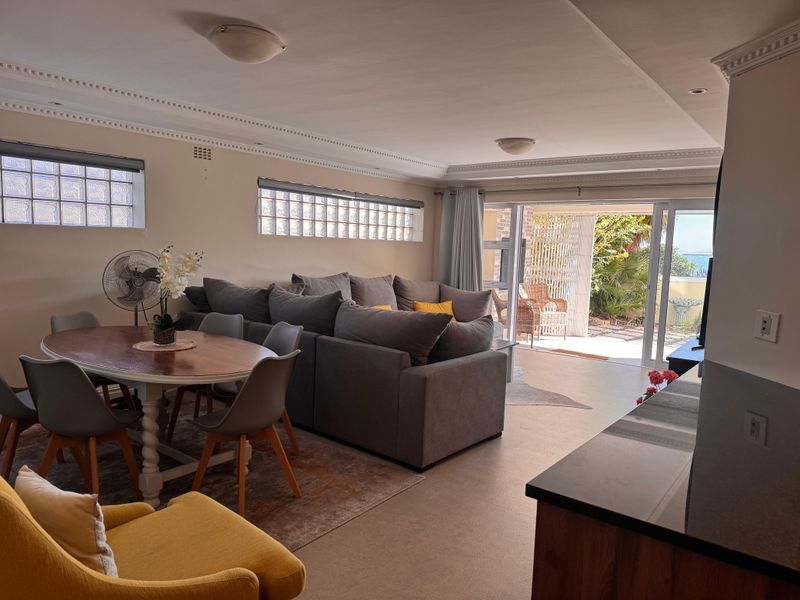 Spacious open-plan living and dining area featuring crown molding, glass block windows, and sliding doors leading to an outdoor patio space.