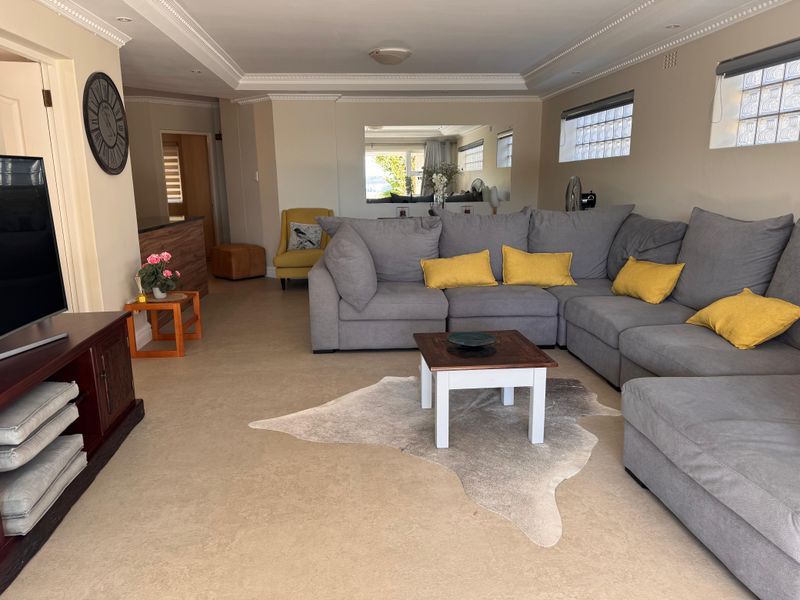 A spacious living room featuring decorative ceiling cornices, recessed lighting, and glass block windows, providing a comfortable and functional lounge area.