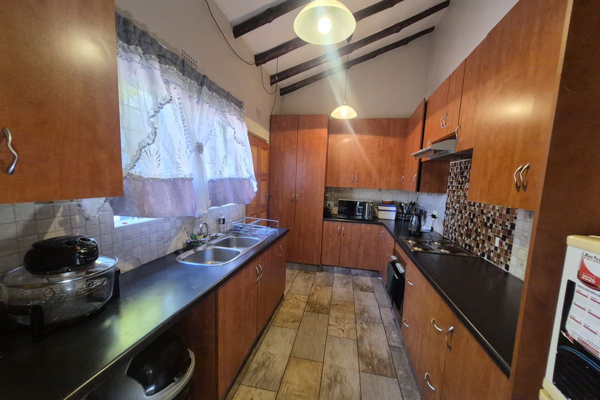 A functional kitchen featuring wooden cabinetry, dark laminate countertops, a mosaic tile backsplash, and exposed ceiling beams, providing a rustic aesthetic.