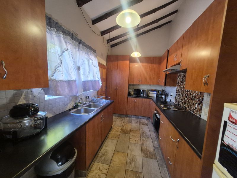 A functional kitchen featuring wooden cabinetry, dark laminate countertops, a mosaic tile backsplash, and exposed ceiling beams, providing a rustic aesthetic.
