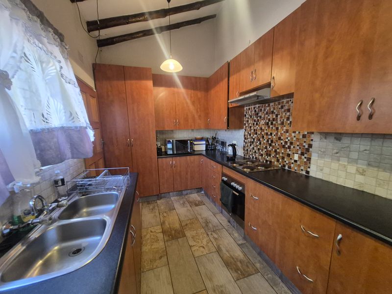 Functional kitchen featuring warm-toned laminate cabinetry, mosaic tile backsplash, built-in oven, electric hob, and exposed timber ceiling beams.