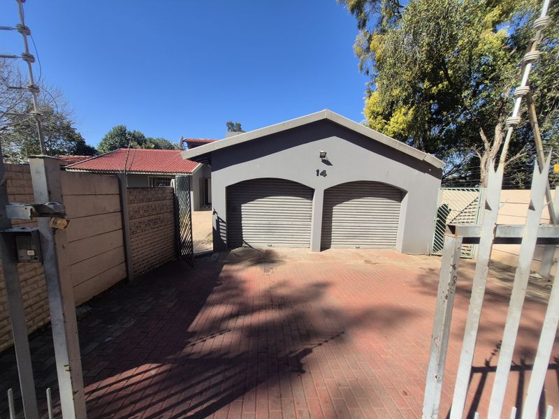Front view of the property featuring a double garage with roller shutter doors, a paved driveway, and secure perimeter fencing.