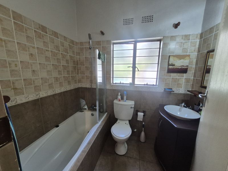 A functional bathroom featuring a bathtub with a glass screen, a vessel sink vanity, and neutral-toned wall and floor tiling.