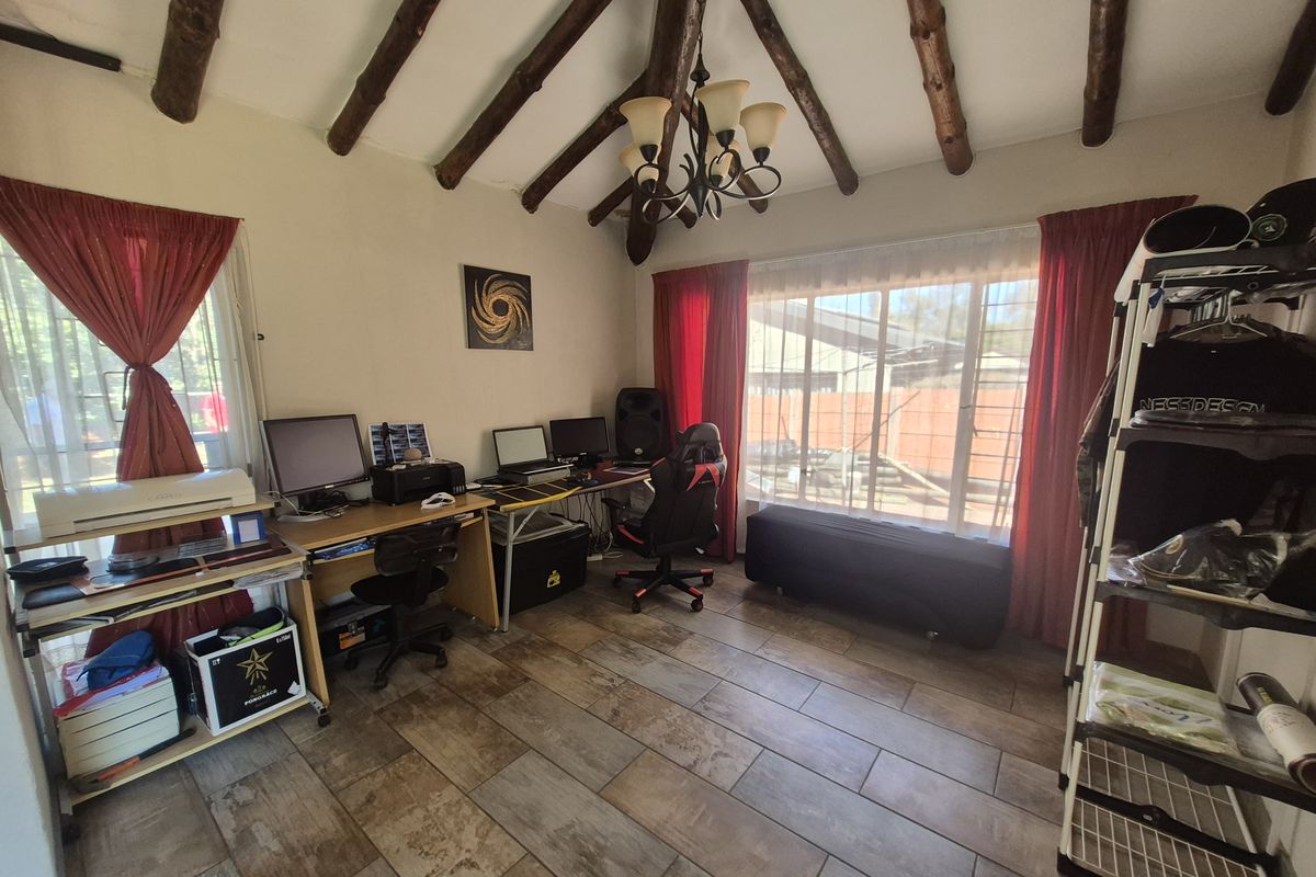A living area featuring rustic exposed timber ceiling beams, tiled flooring, and large windows that provide ample natural light.