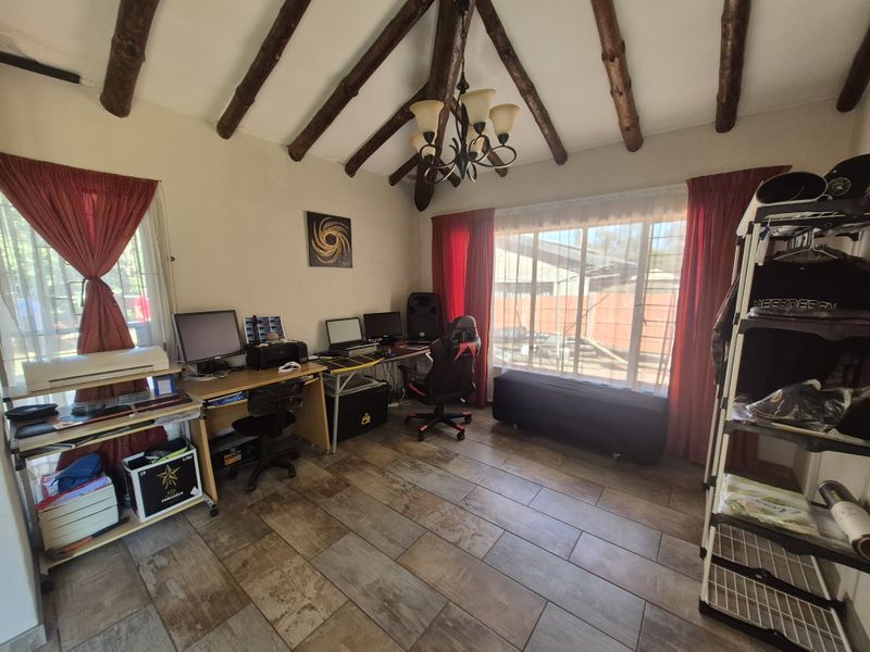 A living area featuring rustic exposed timber ceiling beams, tiled flooring, and large windows that provide ample natural light.