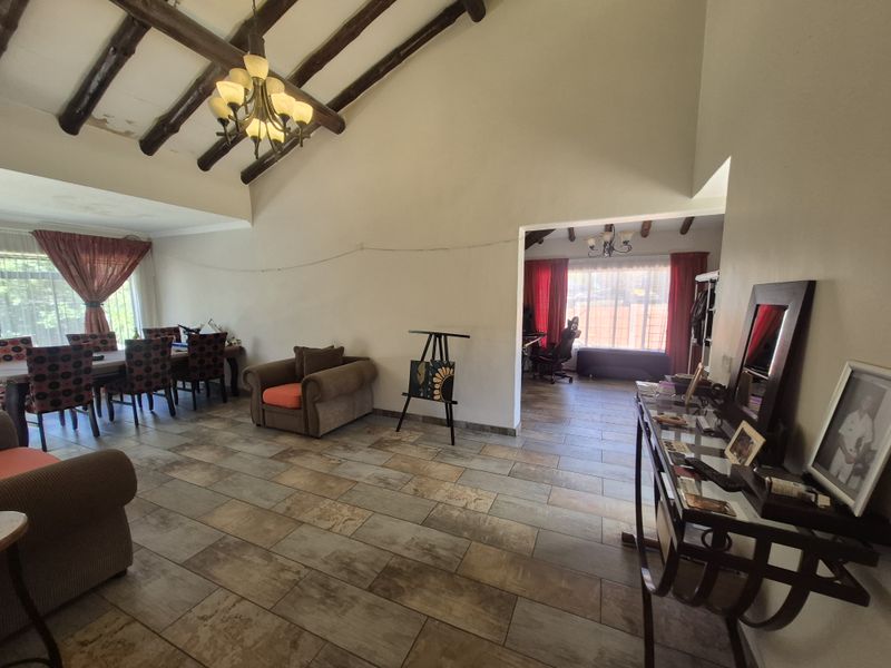 Spacious open-plan living area featuring vaulted ceilings with exposed timber beams, tiled flooring, and a chandelier, connecting to an adjacent room.
