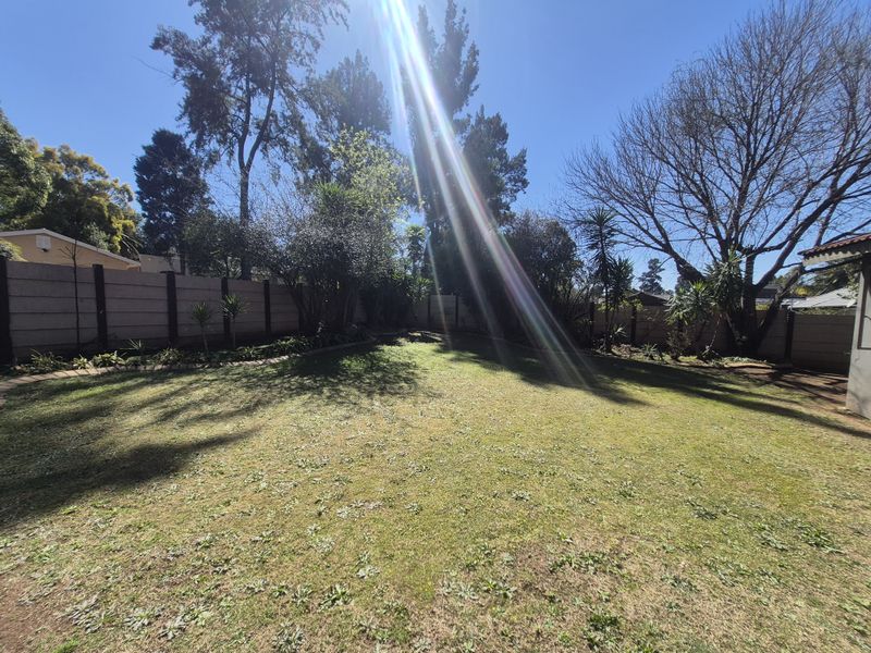 A spacious, level backyard garden featuring a well-defined lawn area enclosed by secure precast concrete boundary walls and mature trees.