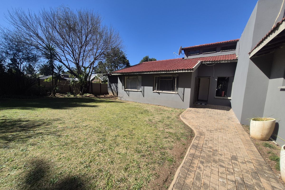 Rear view of the property featuring a paved walkway, lawn area, and a house with terracotta roof tiles and security bars on windows.
