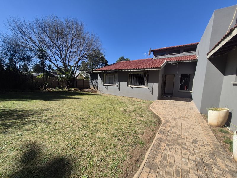 Rear view of the property featuring a paved walkway, lawn area, and a house with terracotta roof tiles and security bars on windows.