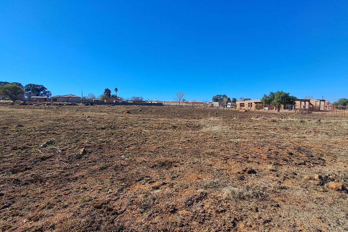 A wide-angle view of a vacant residential plot of land with natural ground cover and perimeter fencing visible in the distance.