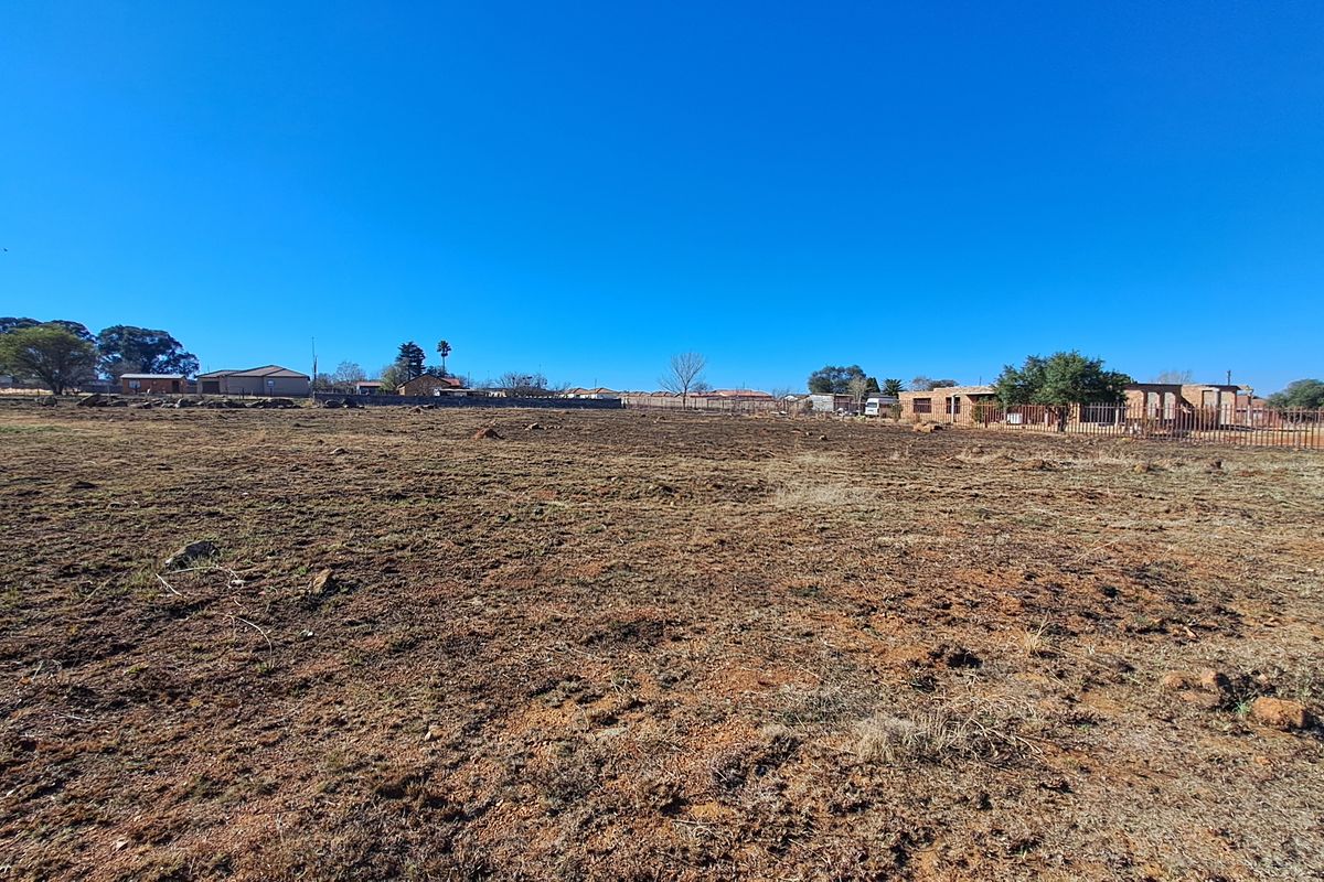 A wide-angle view of a vacant residential plot featuring cleared ground and perimeter fencing, suitable for new development.