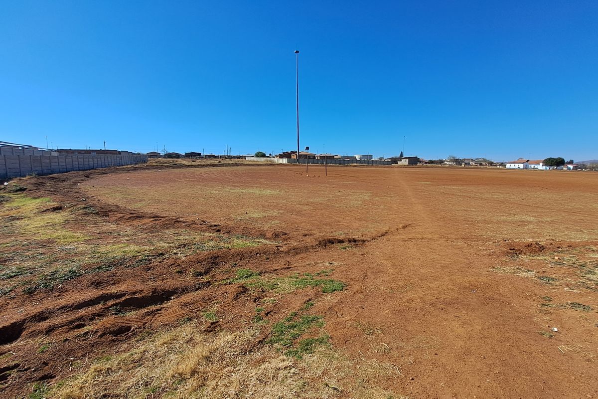 A large, undeveloped vacant residential plot featuring a perimeter wall and a tall floodlight pole, offering significant potential for future development.