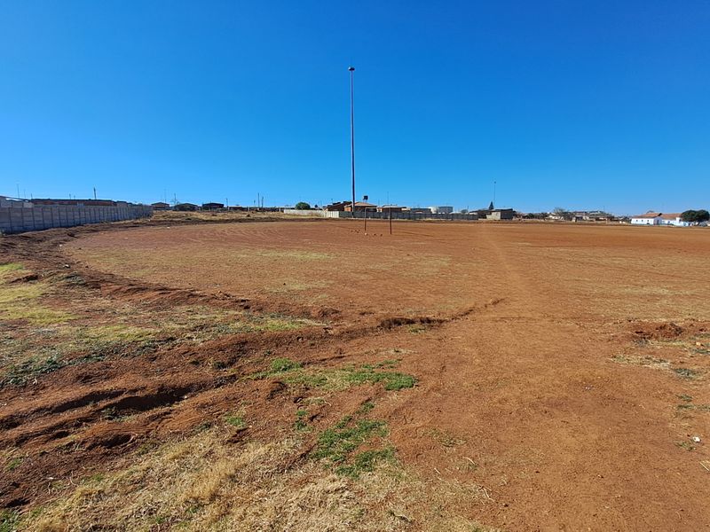 A large, undeveloped vacant residential plot featuring a perimeter wall and a tall floodlight pole, offering significant potential for future development.