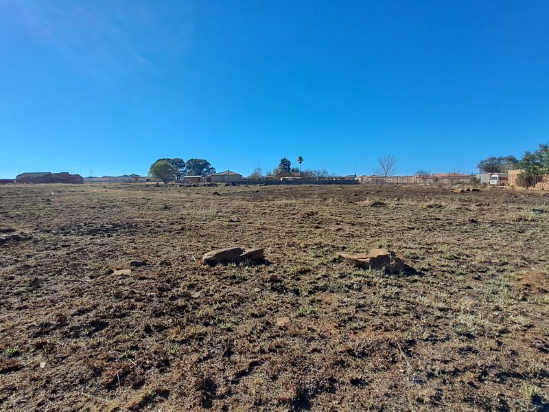 A wide-angle view of a vacant residential plot featuring open land and perimeter fencing, suitable for new development.