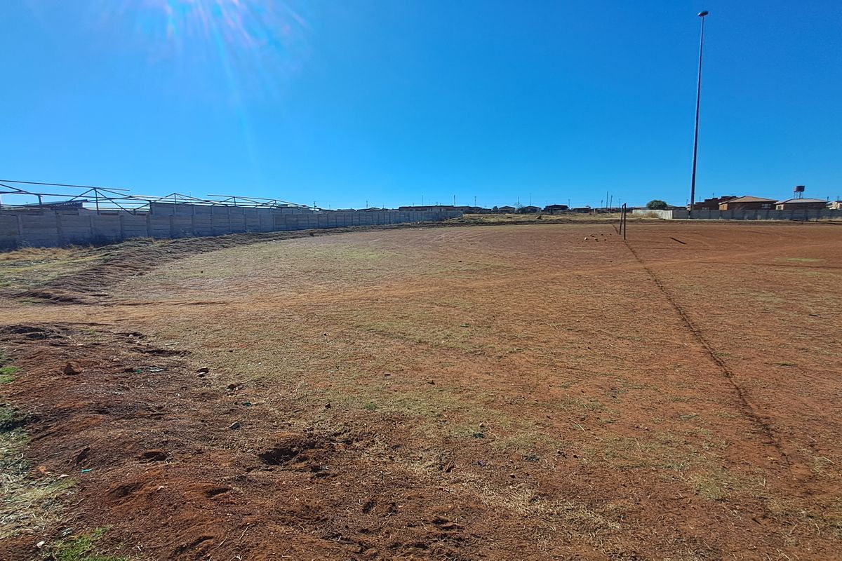 An expansive, undeveloped residential land plot featuring a perimeter wall and a tall floodlight mast, suitable for future development.