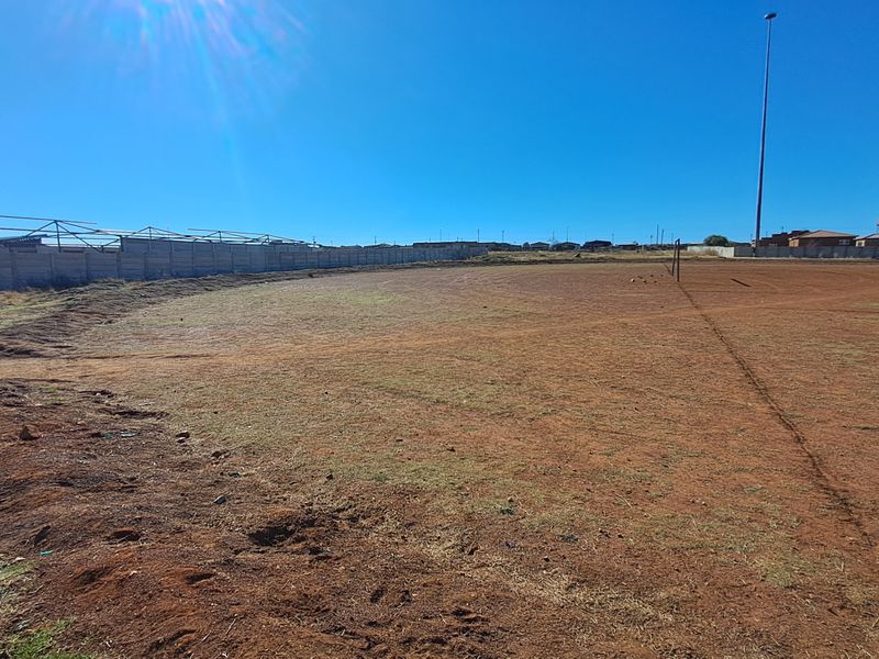 An expansive, undeveloped residential land plot featuring a perimeter wall and a tall floodlight mast, suitable for future development.