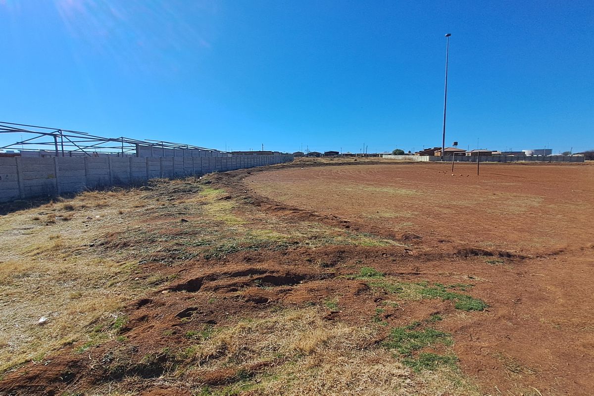 Vacant residential land featuring a precast concrete boundary wall, metal structural framing, and an existing floodlight pole on a large open plot.