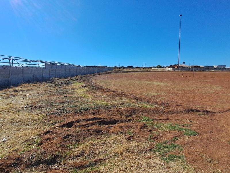 Vacant residential land featuring a precast concrete boundary wall, metal structural framing, and an existing floodlight pole on a large open plot.