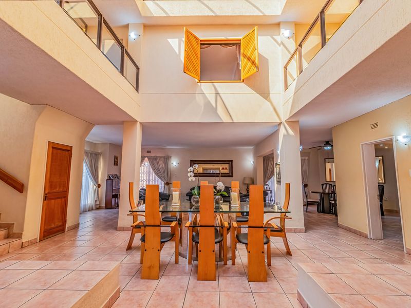 Spacious open-plan living and dining area featuring a double-volume ceiling with a large skylight, tiled flooring, and a mezzanine level overlooking the space.