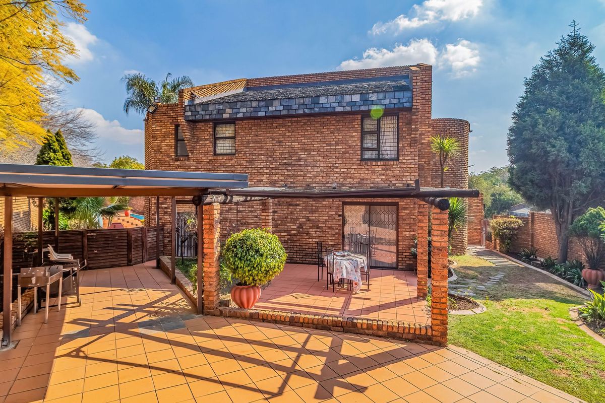Rear view of a brick townhouse featuring a covered patio area, pergola, and established garden space with sliding door access to the interior.