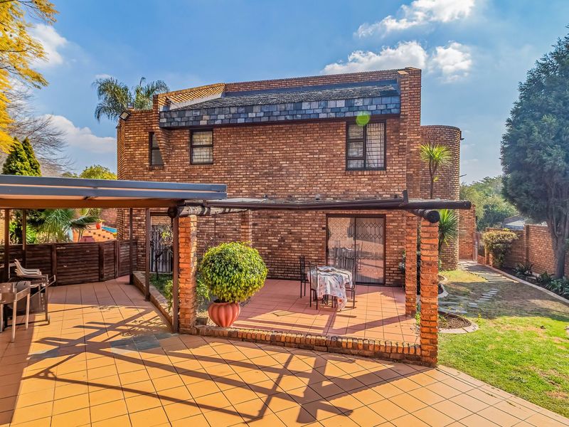 Rear view of a brick townhouse featuring a covered patio area, pergola, and established garden space with sliding door access to the interior.