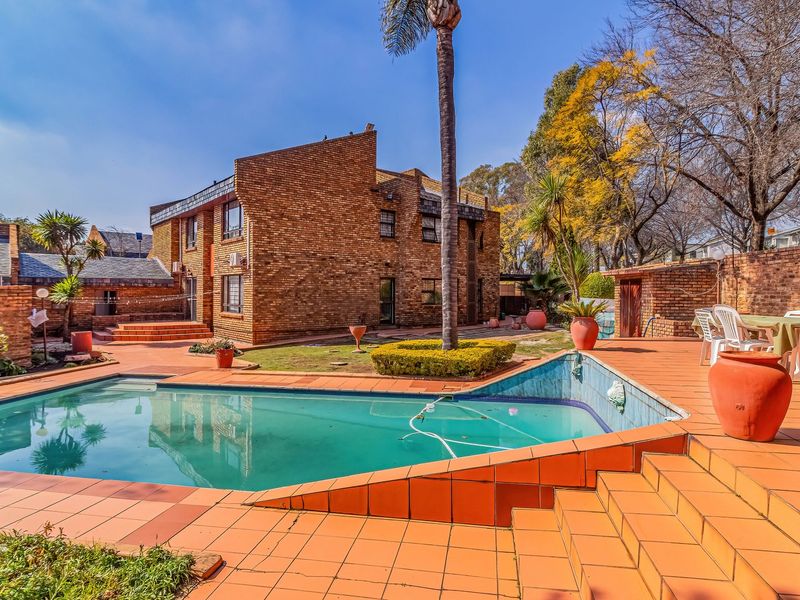Spacious outdoor pool area featuring a tiled deck, brick townhouse exterior, and established garden surroundings, ideal for outdoor entertaining.