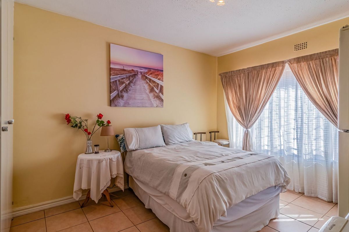 A functional bedroom featuring tiled flooring, a built-in cupboard, and natural light through window curtains.