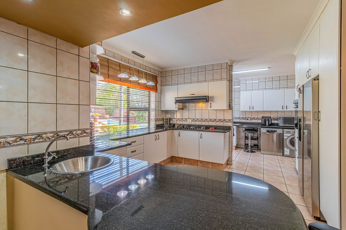 A functional kitchen featuring granite countertops, a gas hob with extractor fan, and ample built-in cabinetry, with an adjoining scullery area.