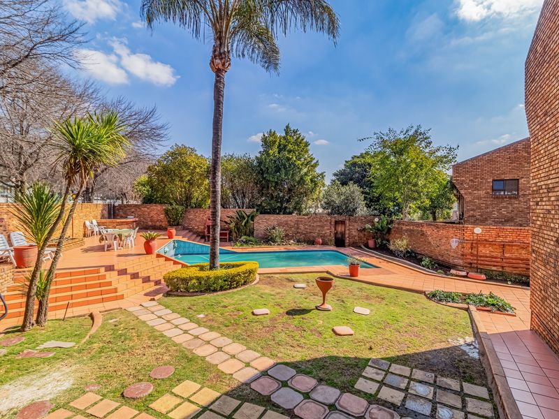 Outdoor pool area featuring a swimming pool, tiled patio, built-in braai, and established garden with brick boundary walls.