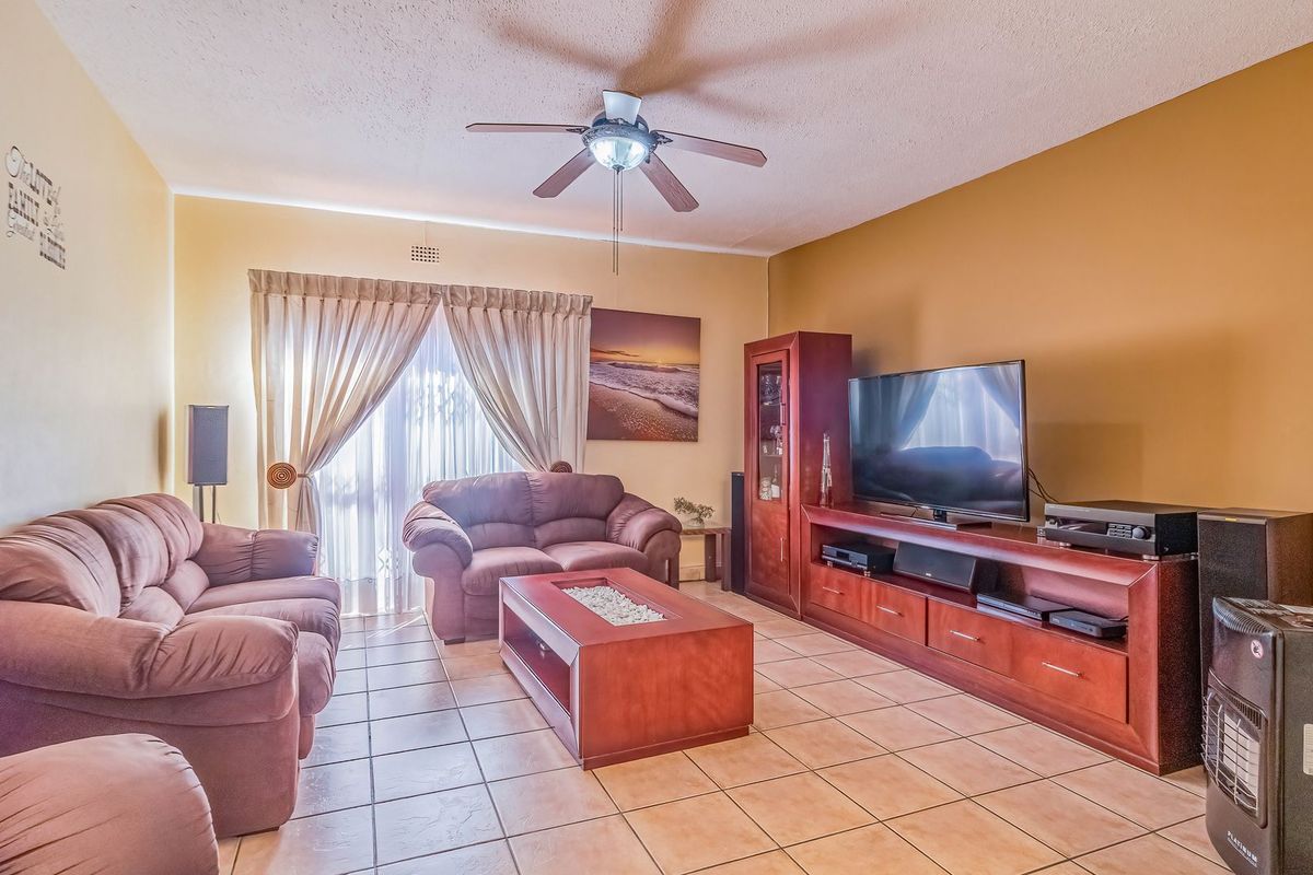 A spacious living room featuring tiled flooring, a ceiling fan, and a sliding glass door providing access to the exterior.