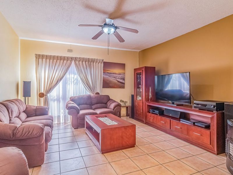 A spacious living room featuring tiled flooring, a ceiling fan, and a sliding glass door providing access to the exterior.