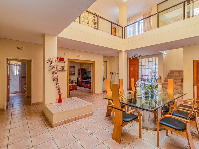 Spacious open-plan living and dining area featuring a double-volume ceiling, mezzanine level, glass block wall, and tiled flooring throughout.