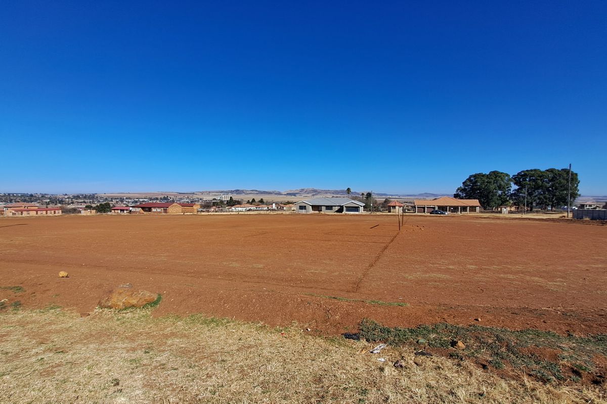 A wide-angle view of a large, level vacant residential plot with surrounding neighborhood views and clear horizon.