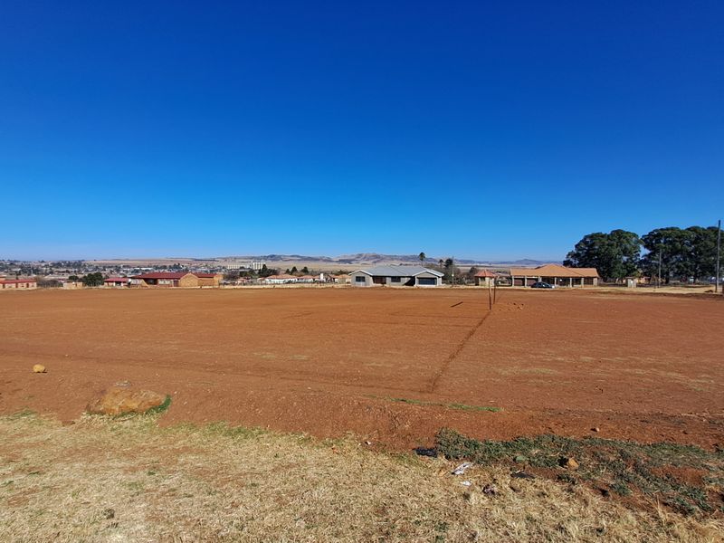 A wide-angle view of a large, level vacant residential plot with surrounding neighborhood views and clear horizon.