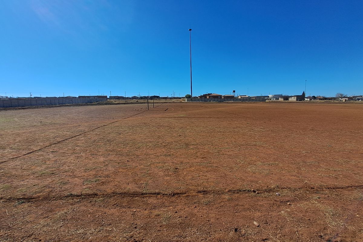 A wide, open vacant residential plot featuring level ground, perimeter walling, and clear views of the surrounding neighborhood.