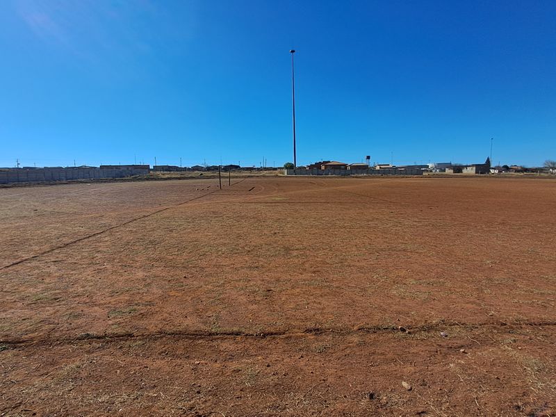 A wide, open vacant residential plot featuring level ground, perimeter walling, and clear views of the surrounding neighborhood.