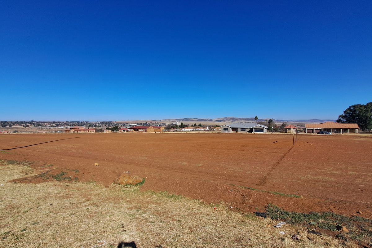 A wide-angle view of a vacant residential plot of land with surrounding neighborhood infrastructure visible in the distance.
