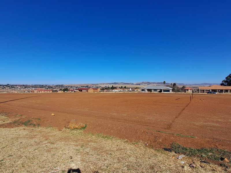 A wide-angle view of a vacant residential plot of land with surrounding neighborhood infrastructure visible in the distance.